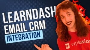 a person wearing a red wp fusion shirt points to the text learndash email crm integration on a blue background. the person has long hair and dark lipstick.